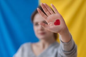 Mujer con un corazón dibujado en la palma de su mano y la bandera de Ucrania de fondo