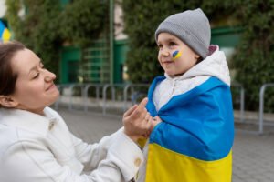 Niño ucraniano envuelto en su bandera mientras su madre lo observa sonrientemente